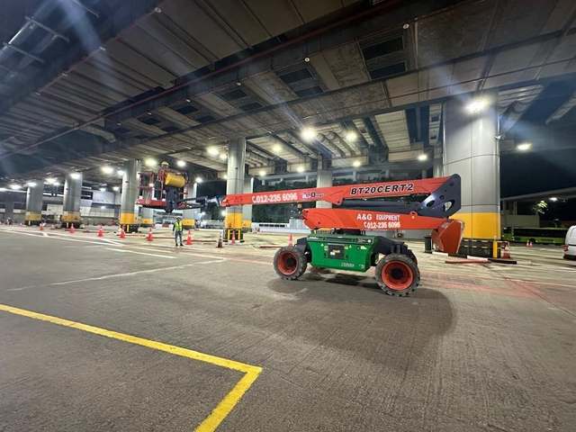 Dingli BT20 boom lift working at height under a covered terminal at night in Johor