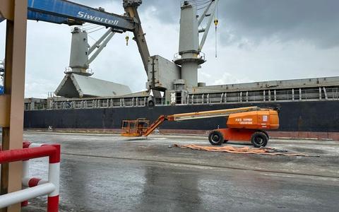 Telescopic boom lift on rental parked on a wharf beside a cargo ship in Johor